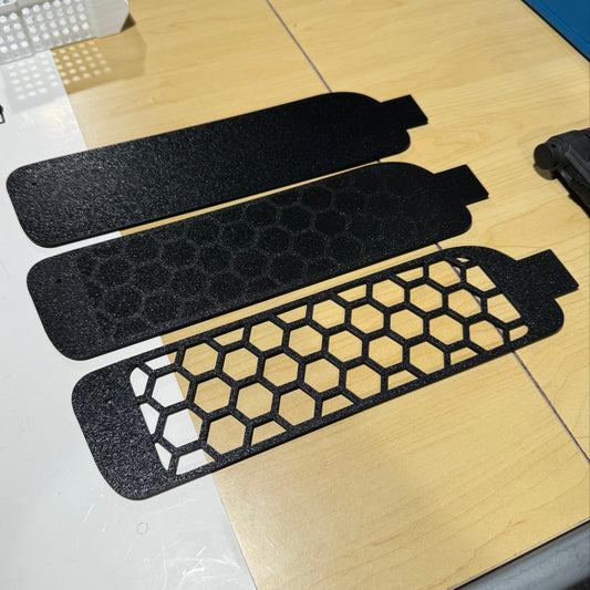 Three black honeycomb-patterned R34 BUMPER VENTS on a wooden surface